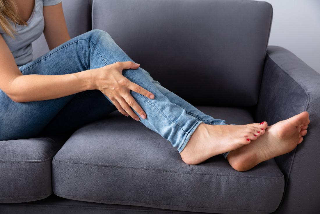 woman on sofa holding leg with muscle strain